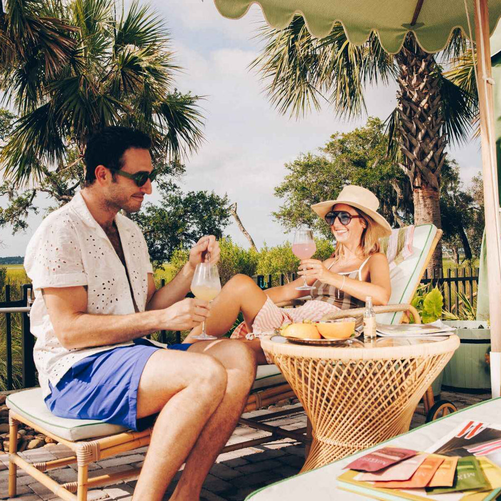 Couple sitting at a table outdoors drinking Mixxers with palm trees and a scenic background