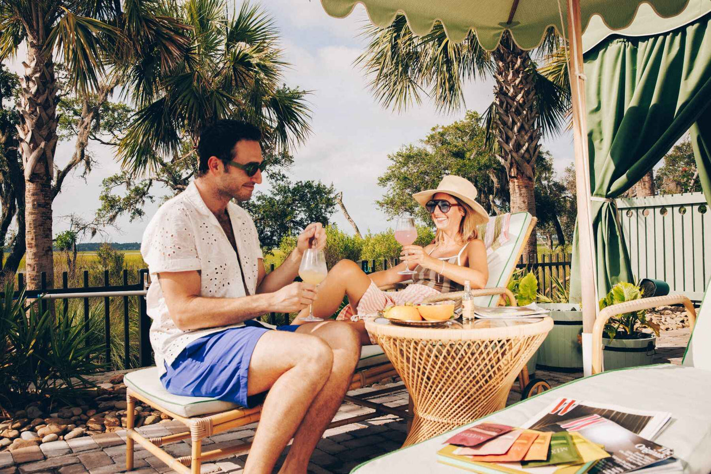Couple sitting at a table outdoors drinking Mixxers with palm trees and a scenic background