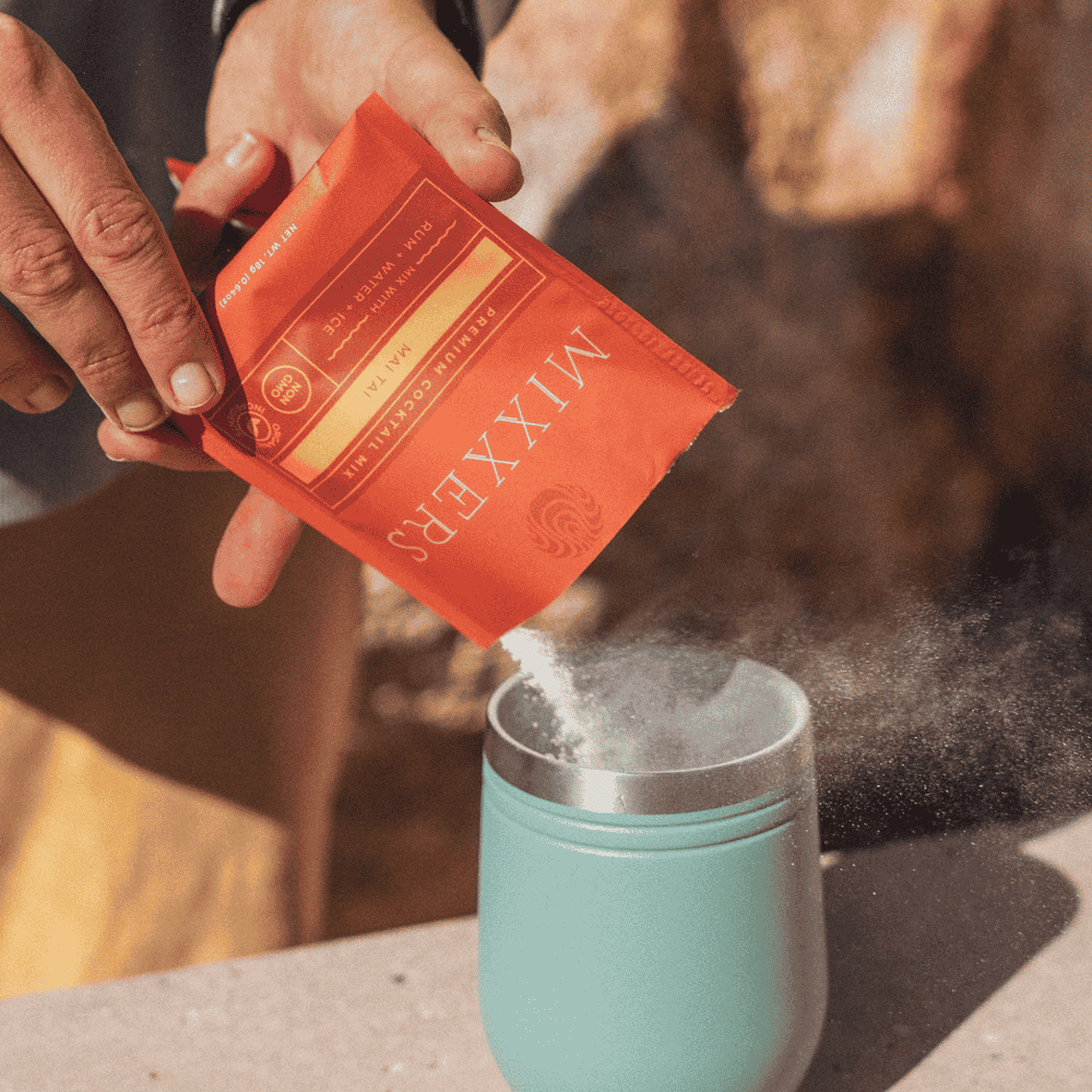 Person pouring a red packet of Mixxers into a teal mug with steam rising.